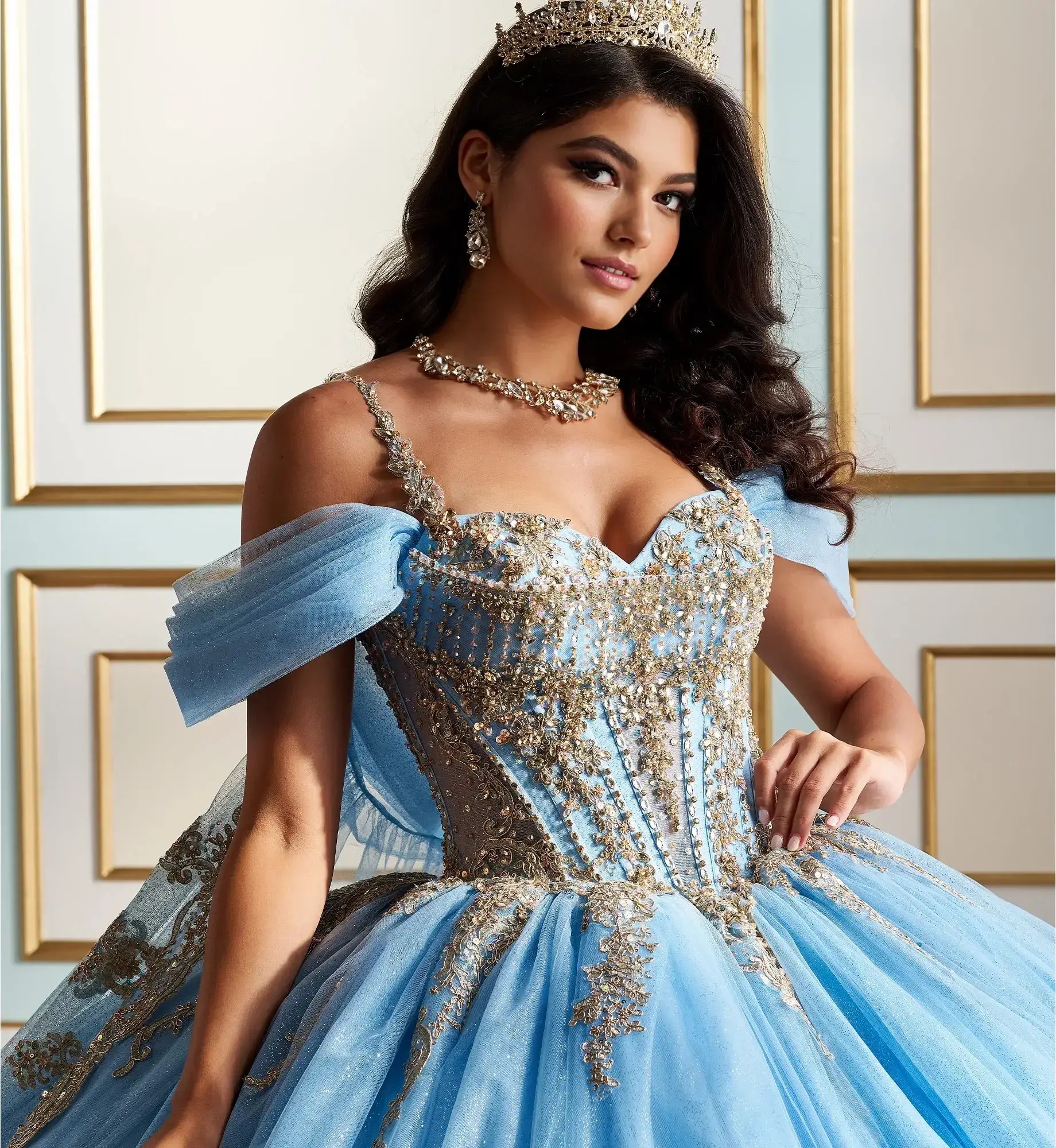 La modelo lleva un vestido de quinceañera azul claro con dorado y mangas caídas