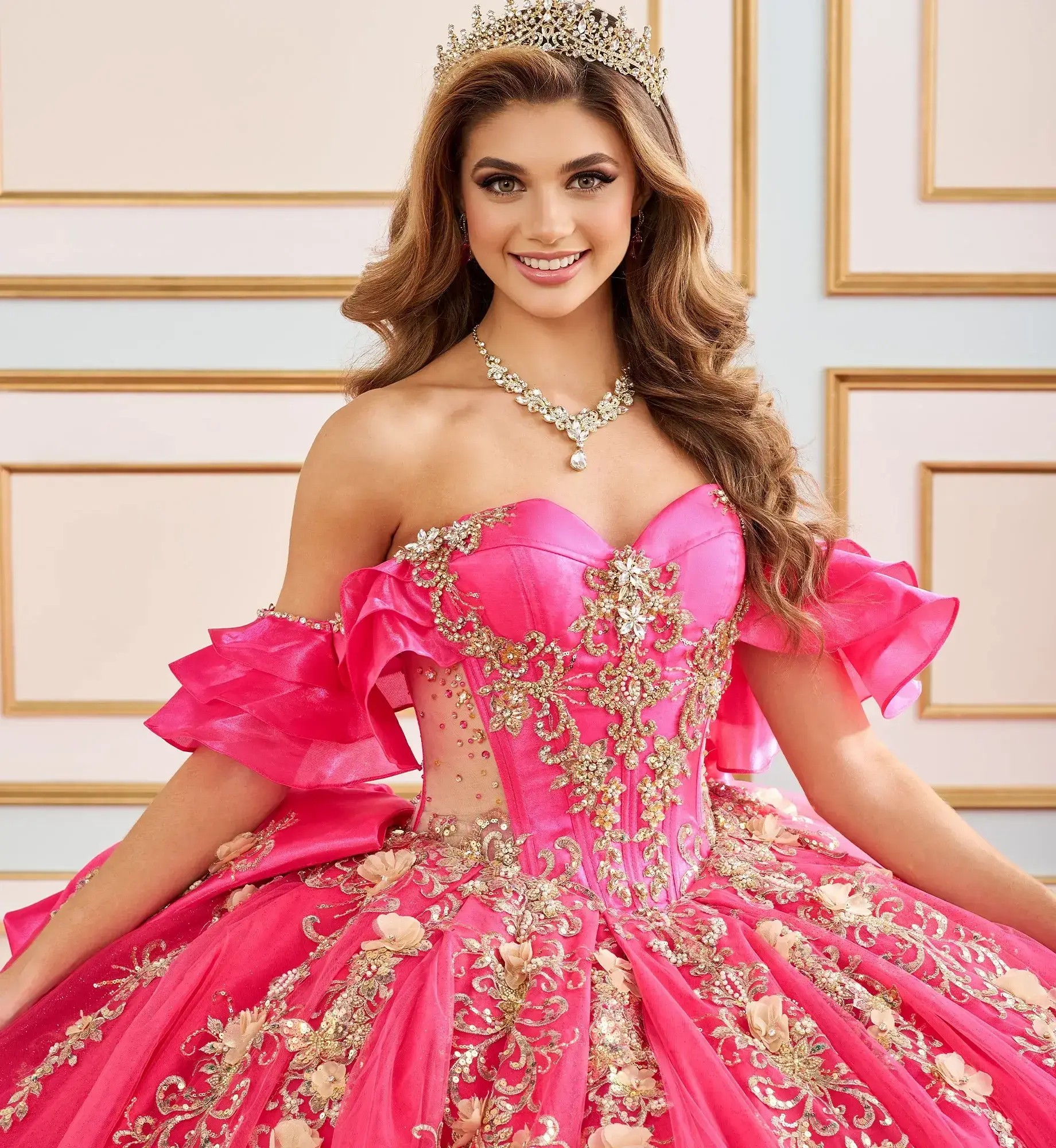 La modelo lleva un vestido de quinceañera fucsia con dorado y escote caído sobre los hombros