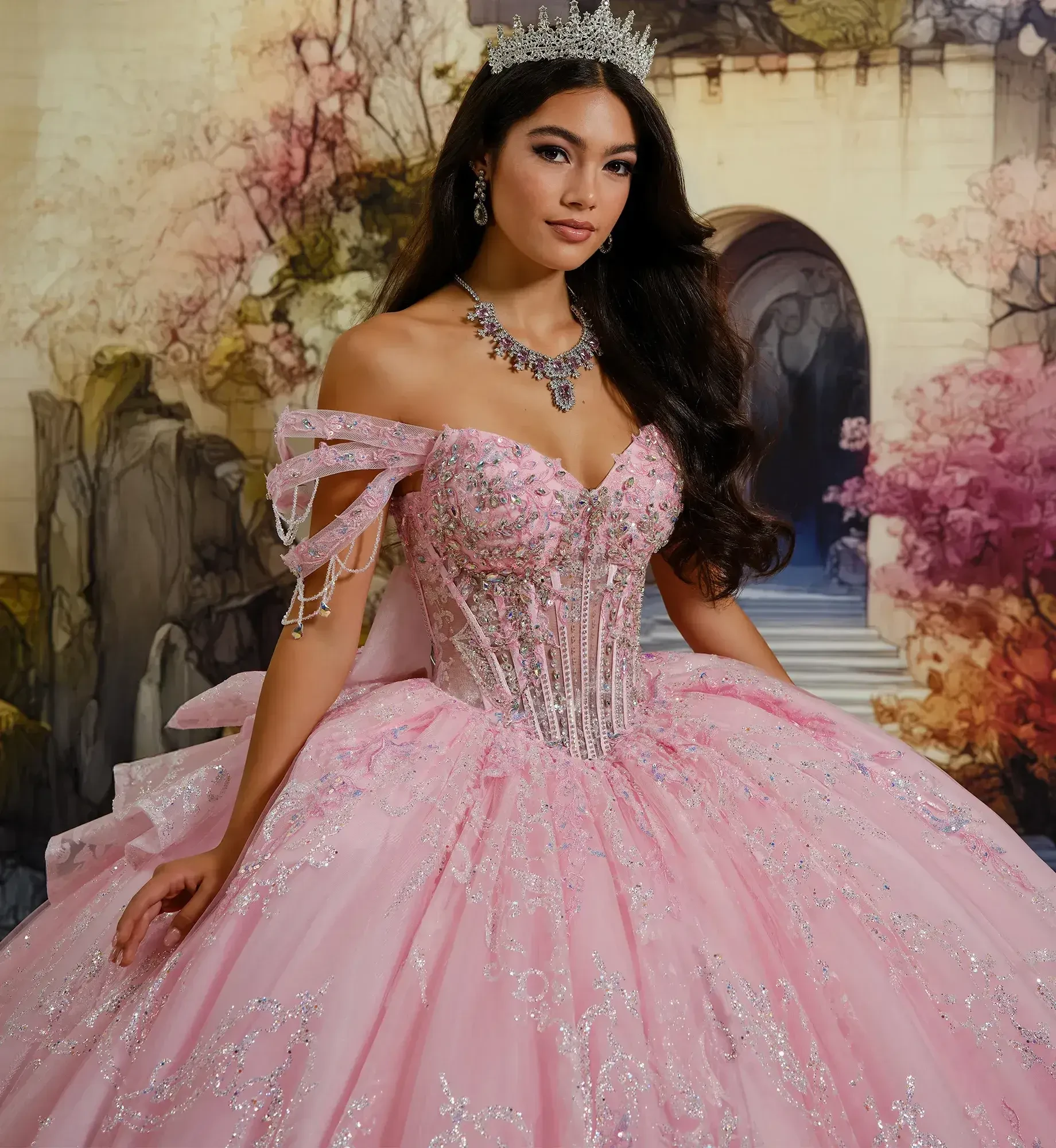 Una mujer con un brillante vestido de gala rosa se yergue sonriendo frente a un tel&oacute;n de fondo de cuento de hadas con arcos y v&iacute;vidos &aacute;rboles oto&ntilde;ales, exudando elegancia.