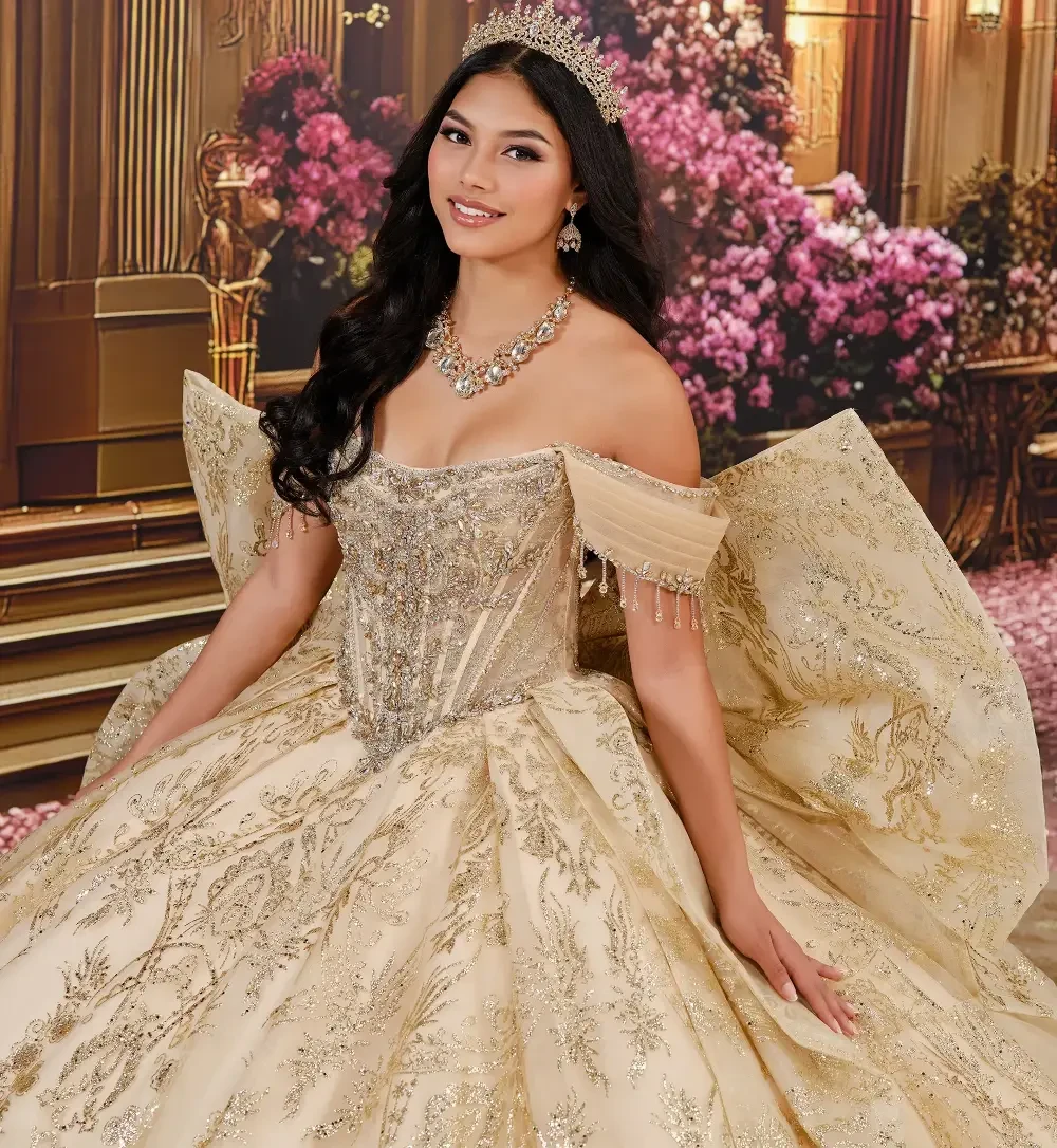 Una mujer que viste un lujoso y ornamentado vestido dorado se encuentra en un entorno elegante, con grandes puertas y decoraciones florales.