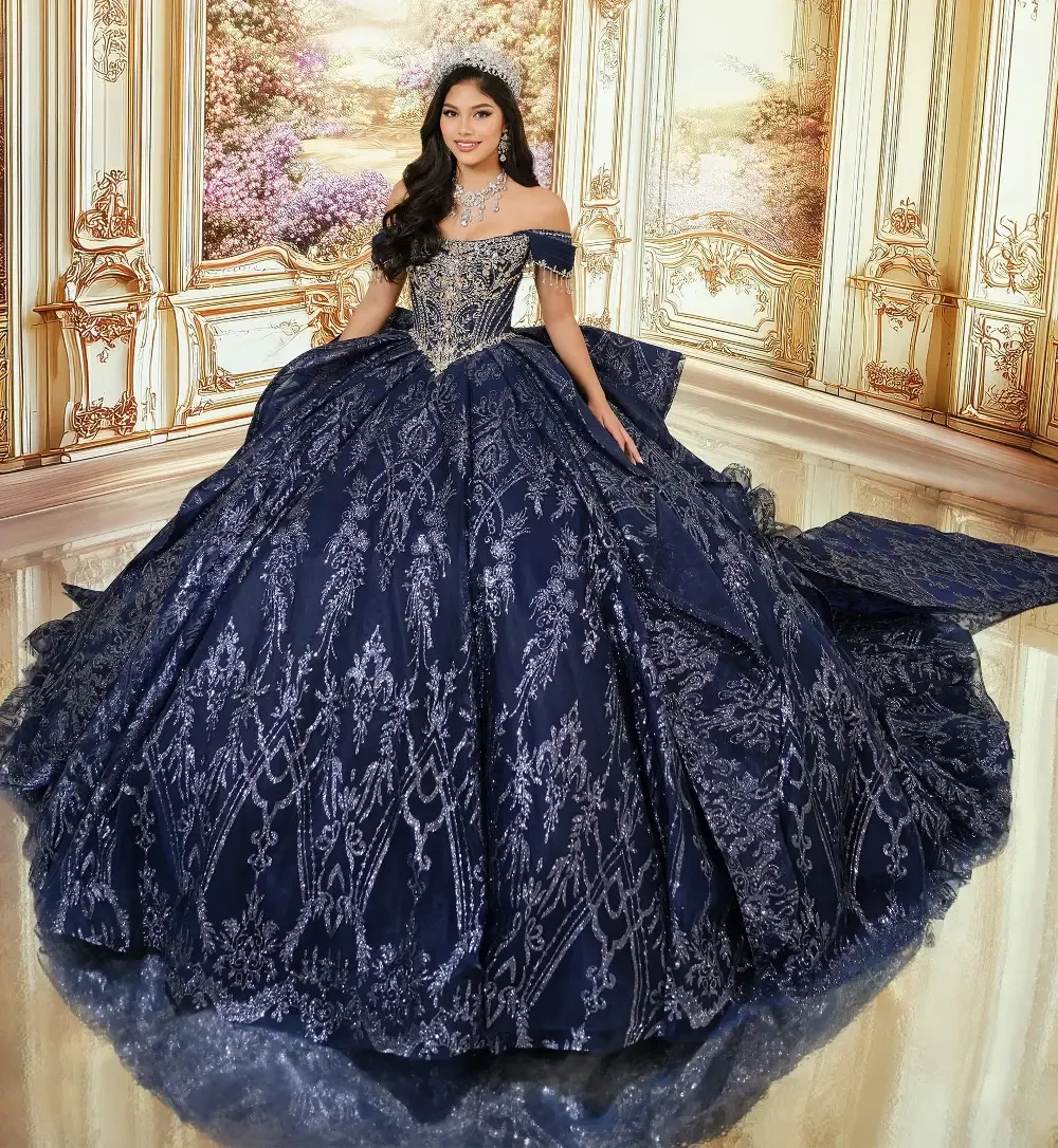 Una joven, vestida con un elegante y ornamentado traje azul marino, se encuentra con gracia en una estancia suntuosa de decoraci&oacute;n elaborada y grandes ventanales. El vestido luce un intrincado bordado en plata y una falda vaporosa, lo que le confiere un aire majestuoso.
