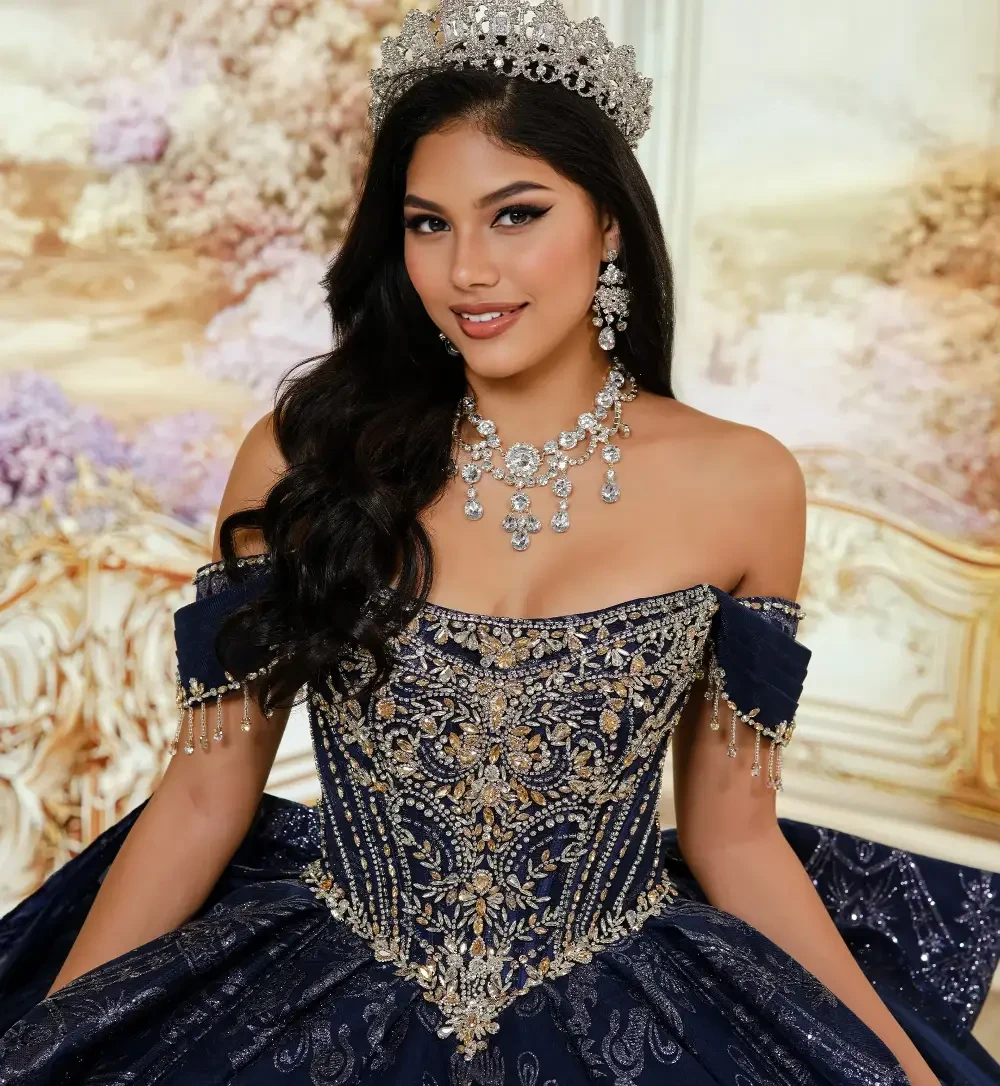 Una joven, vestida con un elegante y ornamentado traje azul marino, se encuentra con gracia en una estancia suntuosa de decoraci&oacute;n elaborada y grandes ventanales. El vestido luce un intrincado bordado en plata y una falda vaporosa, lo que le confiere un aire majestuoso.